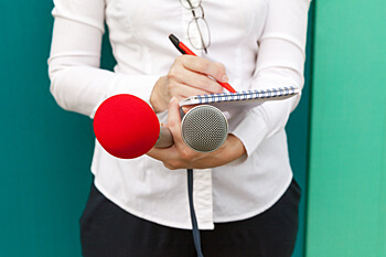Person hält Notizblock und Mikrofone in der Hand